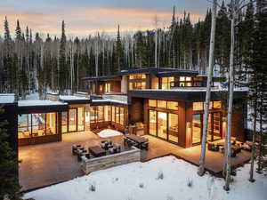 Snow covered house with a patio area, an outdoor living space with a fire pit, and a wooded view