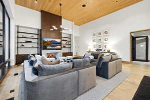 Living area featuring a high ceiling, wood ceiling, a warm lit fireplace, built in features, and light wood-type flooring
