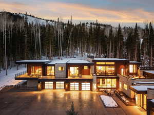 Back of property at dusk featuring stone siding, a view of trees, and a patio area