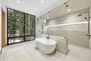 Bathroom featuring a wall of windows, a tile shower, a freestanding bath, and tile walls