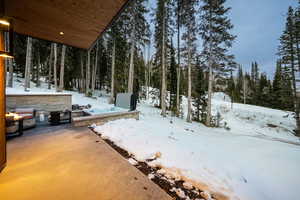 Yard layered in snow with an outdoor fire pit and a wooded view