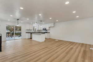 Kitchen with white cabinetry, hanging light fixtures, stainless steel appliances, a kitchen island, and light wood-type flooring