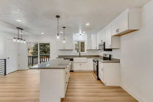 Kitchen featuring appliances with stainless steel finishes, a center island, hanging light fixtures, and white cabinets