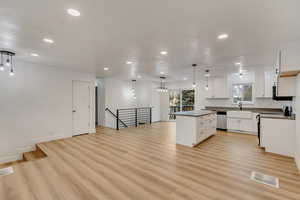 Kitchen featuring a center island, light wood-type flooring, stainless steel dishwasher, pendant lighting, and white cabinets