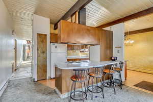 Kitchen featuring a kitchen bar, kitchen peninsula, white appliances, beam ceiling, and a baseboard heating unit