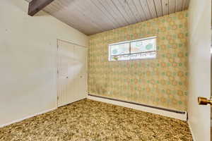 Unfurnished bedroom with vaulted ceiling with beams, a baseboard radiator, a closet, and wooden ceiling