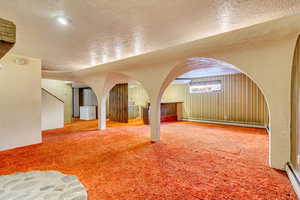 Additional living space with a baseboard heating unit, carpet floors, and a textured ceiling