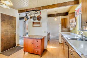 Kitchen with sink, light hardwood / wood-style flooring, hanging light fixtures, and beamed ceiling