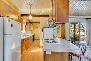 Kitchen featuring sink, hanging light fixtures, light hardwood / wood-style flooring, beamed ceiling, and white appliances