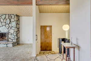 Carpeted entrance foyer featuring wood ceiling, a fireplace, and lofted ceiling with beams