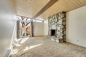 Unfurnished living room featuring light colored carpet, a stone fireplace, beam ceiling, and wooden ceiling