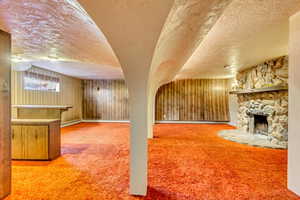 Unfurnished living room with a stone fireplace, carpet floors, and a textured ceiling