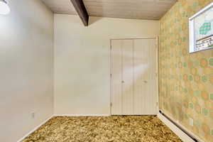 Unfurnished bedroom with wood ceiling, beam ceiling, carpet, a baseboard radiator, and a closet