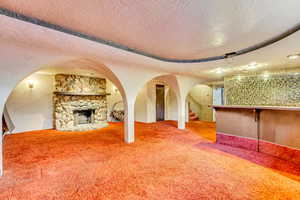 Unfurnished living room featuring a stone fireplace, a textured ceiling, and carpet