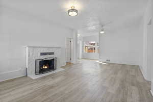 Unfurnished living room featuring a fireplace, ceiling fan, light hardwood / wood-style floors, and a textured ceiling