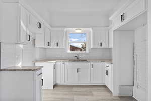 Kitchen featuring white cabinetry, sink, decorative backsplash, and light hardwood / wood-style flooring