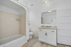 Full bathroom featuring toilet, tile walls, tiled shower / bath, wood-type flooring, and vanity