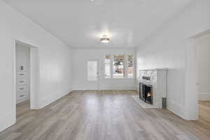 Unfurnished living room featuring light hardwood / wood-style flooring, a stone fireplace, and a textured ceiling