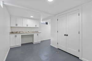 Interior space featuring white cabinetry, built in desk, and light stone counters