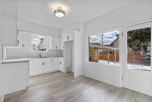 Kitchen with light hardwood / wood-style flooring, sink, white cabinetry, and decorative backsplash