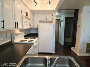 Kitchen featuring backsplash, white appliances, dark hardwood / wood-style floors, and white cabinets