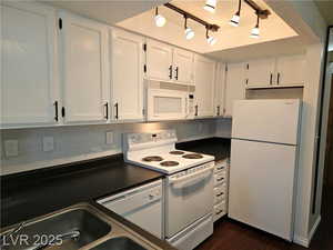 Kitchen with tasteful backsplash, white cabinetry, sink, dark wood-type flooring, and white appliances