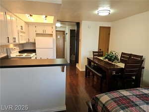 Kitchen featuring dark hardwood / wood-style floors, white cabinets, white appliances, kitchen peninsula, and a textured ceiling