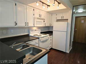 Kitchen with sink, white appliances, dark wood-type flooring, white cabinetry, and backsplash