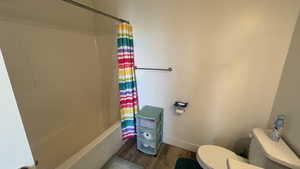 Bathroom with wood-type flooring, toilet, and shower / bath combo with shower curtain