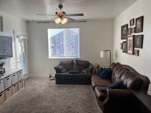 Carpeted living room featuring ceiling fan and a textured ceiling