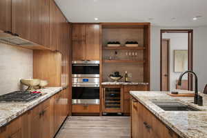 Kitchen featuring appliances with stainless steel finishes, sink, beverage cooler, light stone countertops, and light wood-type flooring