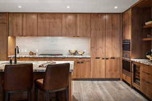 Kitchen with sink, a kitchen breakfast bar, light stone counters, tasteful backsplash, and light wood-type flooring