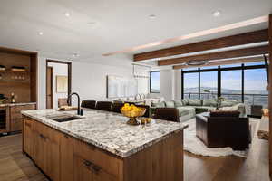 Kitchen with dark hardwood / wood-style flooring, a kitchen island with sink, sink, and light stone counters