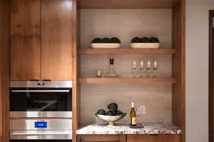 Bar with decorative backsplash, light stone countertops, and stainless steel double oven