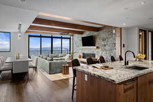 Kitchen featuring dark hardwood / wood-style floors, a fireplace, sink, light stone countertops, and a center island with sink