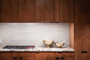 Kitchen featuring light stone counters, stainless steel gas stovetop, and backsplash