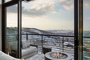 Snow covered back of property with a mountain view and an outdoor fire pit