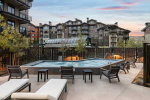 Pool at dusk featuring pool water feature, a jacuzzi, and a patio area