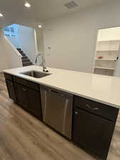 Kitchen featuring stainless steel dishwasher, a kitchen island with sink, sink, and light wood-type flooring