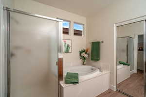 Bathroom with a textured ceiling, wood finished floors, a shower stall, and a bath