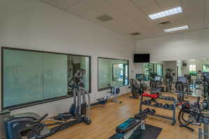 Workout area with light wood-style floors, a paneled ceiling, visible vents, and a high ceiling