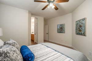 Carpeted bedroom featuring arched walkways, ceiling fan, ensuite bathroom, and baseboards