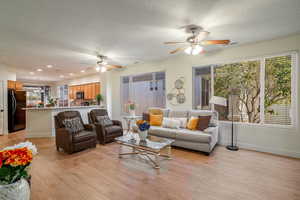 Living room featuring light wood finished floors, baseboards, a ceiling fan, a textured ceiling, and recessed lighting