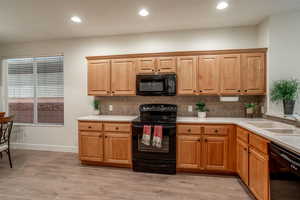 Kitchen featuring decorative backsplash, light countertops, light wood-type flooring, black appliances, and a sink