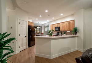 Kitchen featuring light wood-style flooring, a peninsula, light countertops, black appliances, and pendant lighting