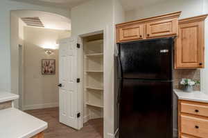 Kitchen with arched walkways, wood finished floors, light countertops, freestanding refrigerator, and decorative backsplash