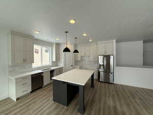 Kitchen with pendant lighting, appliances with stainless steel finishes, dark hardwood / wood-style floors, tasteful backsplash, and a kitchen island