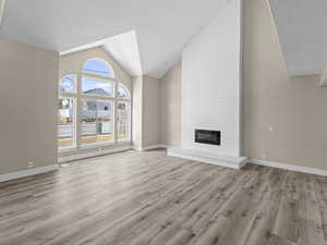 Unfurnished living room featuring high vaulted ceiling, light hardwood / wood-style floors, and a large fireplace