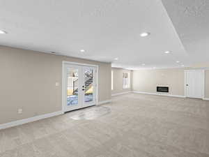 Unfurnished living room featuring light colored carpet, a textured ceiling, and french doors