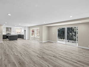 Unfurnished living room with sink, a textured ceiling, and light wood-type flooring